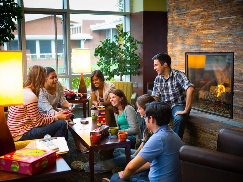 Group of students sitting in front of a fireplace playing board games.