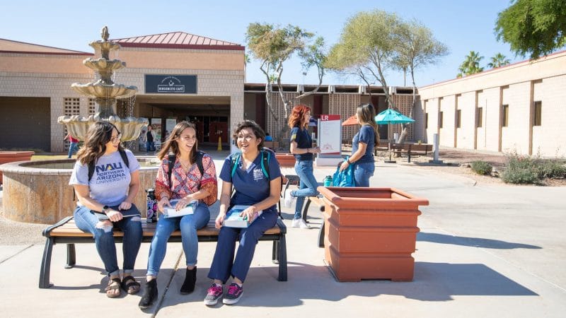 Three students sit on bench outside.