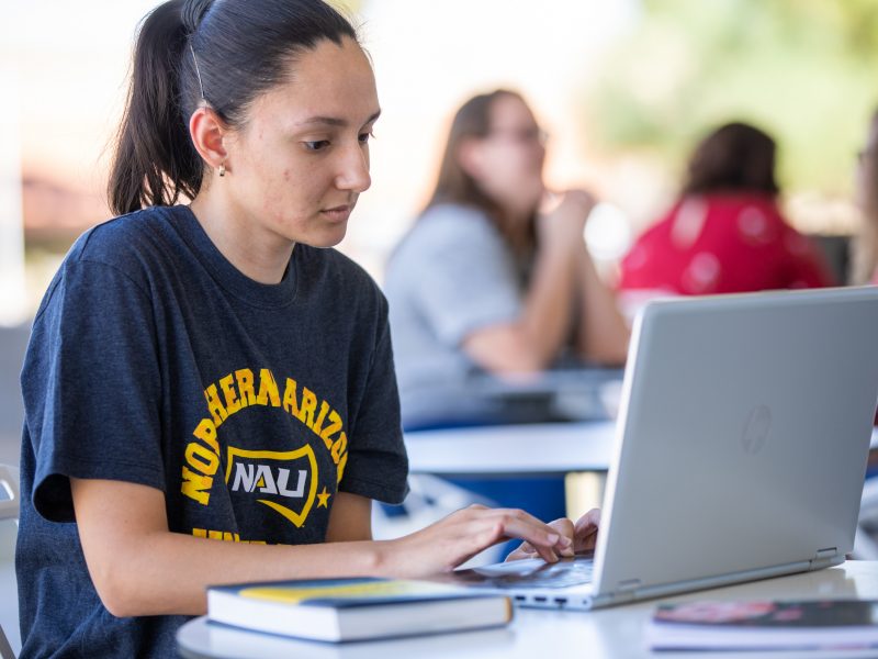 Student working on a computer at a table outside.